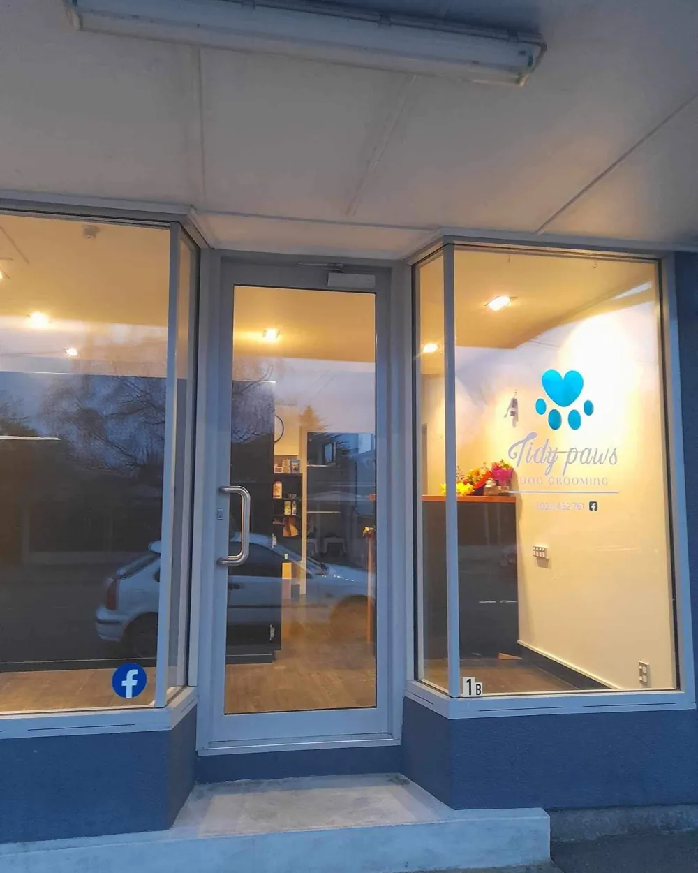 The Tidy Paws shopfront at 1B Cossar Street, with warm lights on inside and the teal heart paw decal on the window